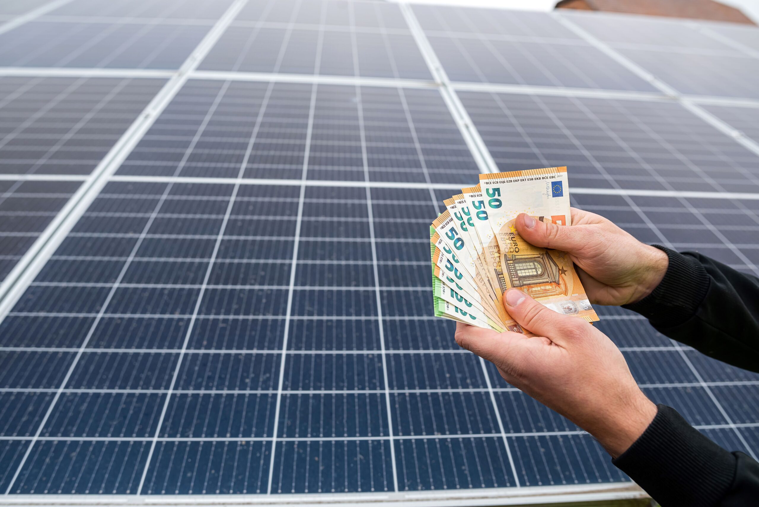 Eine Person hält Geld in der Hand vor einer Solaranlage 