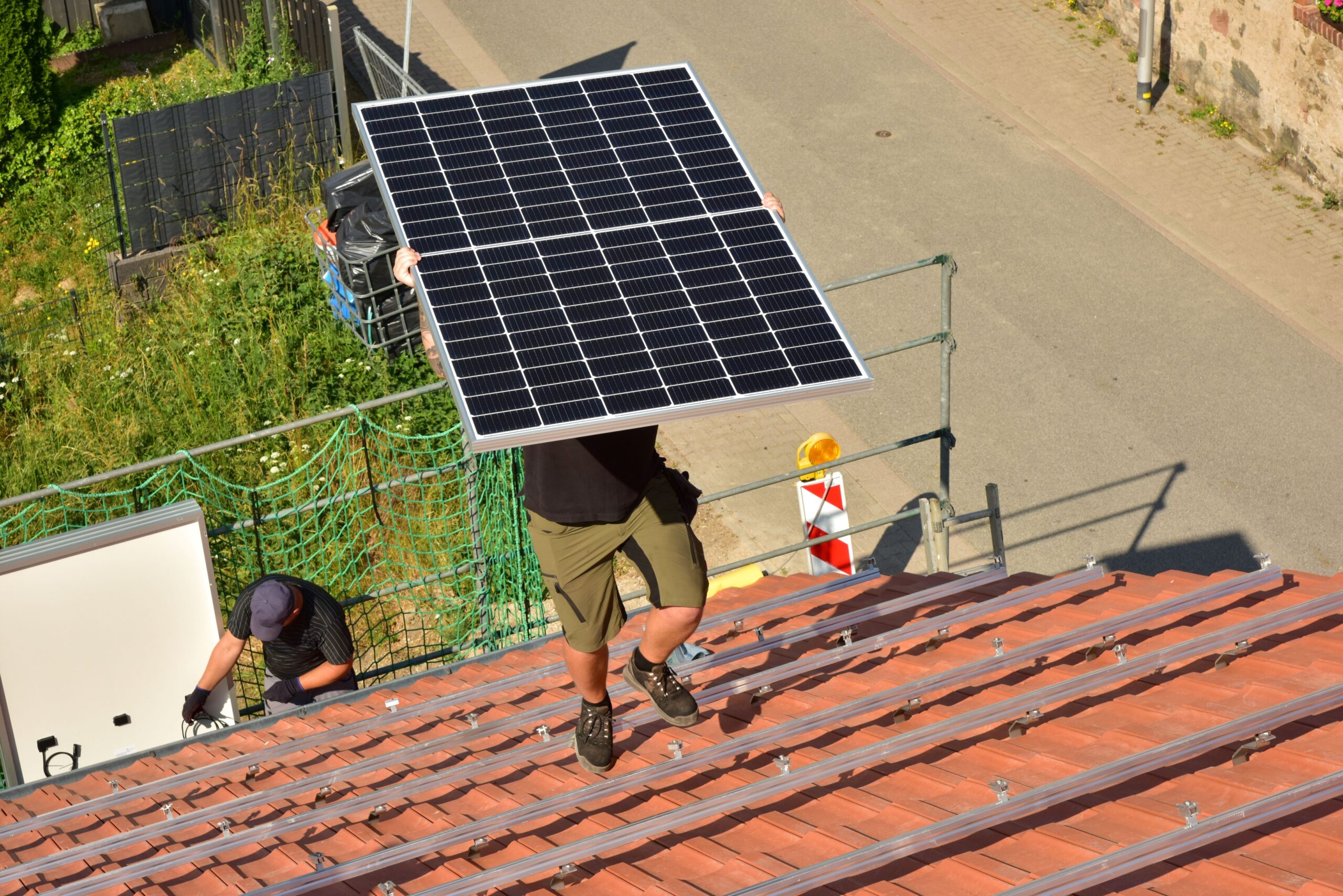 Eine Person trägt eine Solarzelle auf ein Dach hoch um diese auf dem Dach anzubringen 