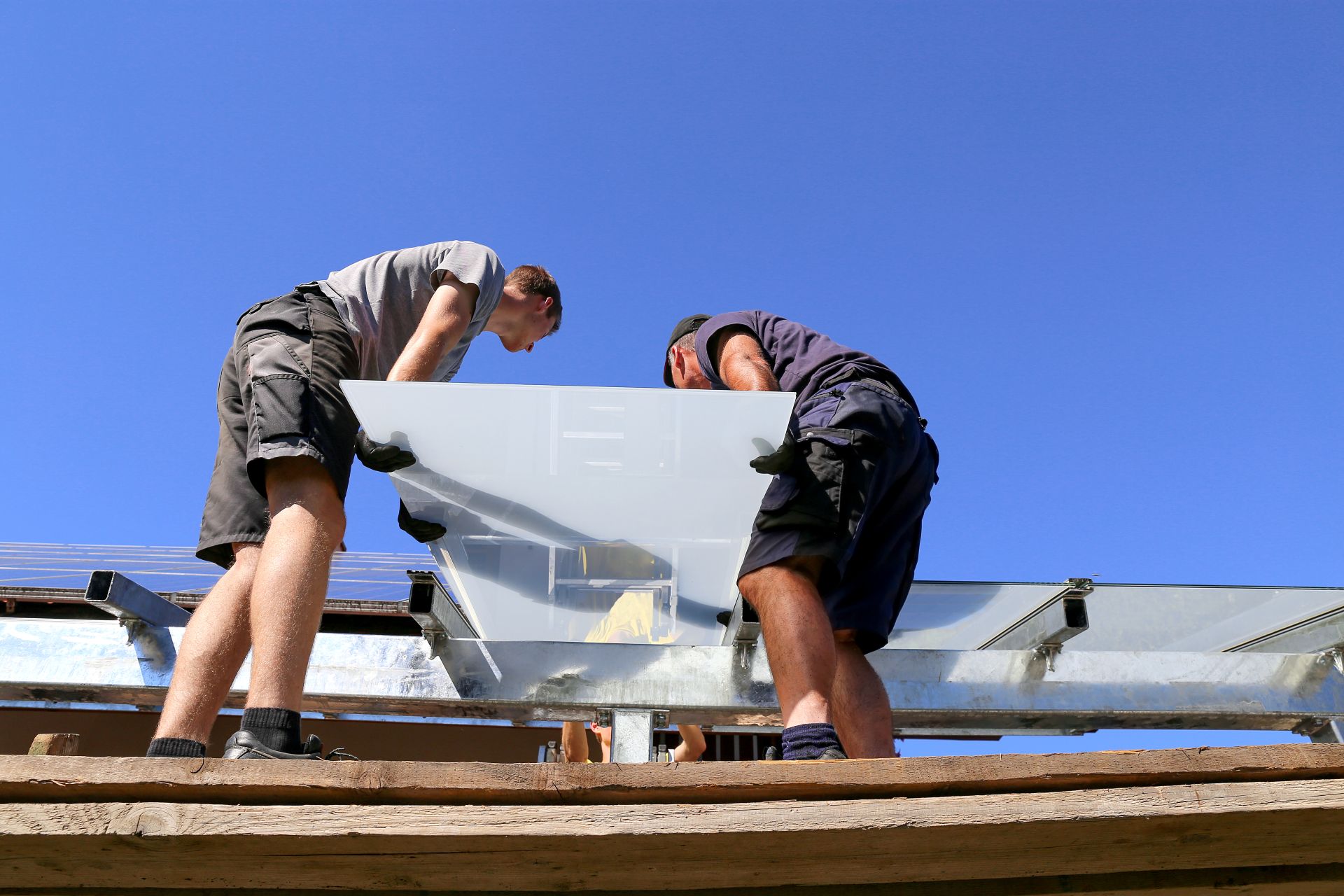 Zwei Handwerker montieren eine Glasplatte für eine neue Terrassenüberdachung unter freiem Himmel